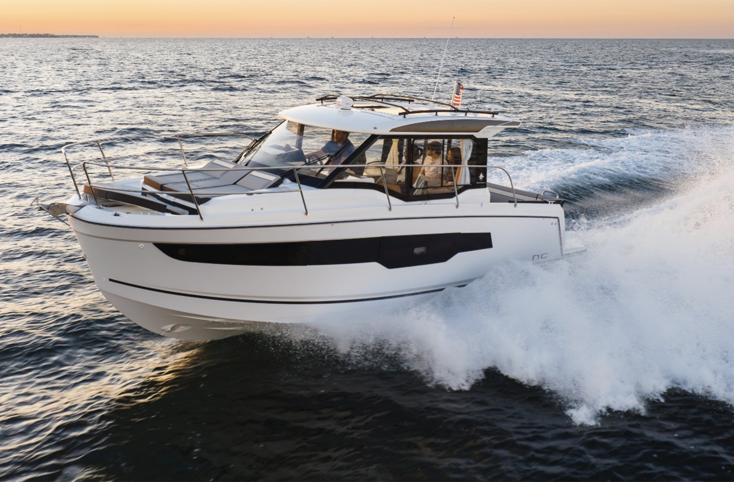 A white Jeanneau NC 895 Series 2 powerboat cruising through choppy ocean waters at speed, leaving a large white wake behind under a warm twilight sky.