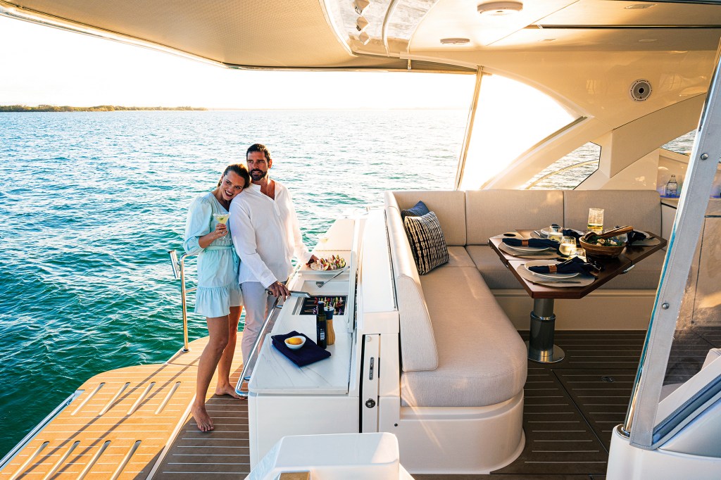 A couple enjoying drinks and grilling on the aft deck and swim platform of a luxury yacht during golden hour.
