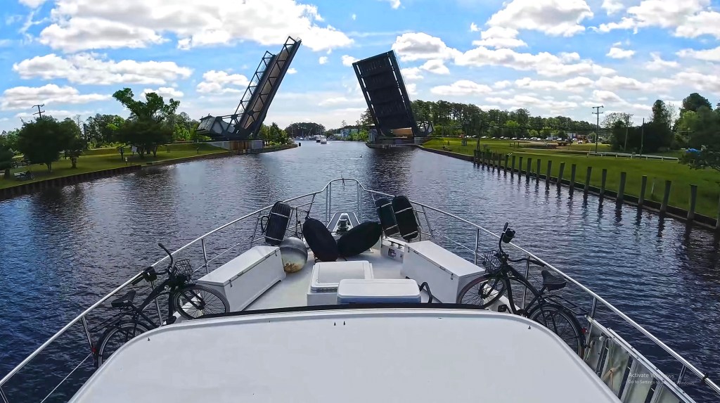A view from the bow of a boat with bicycles attached to the railing as it approaches an open drawbridge over a canal.