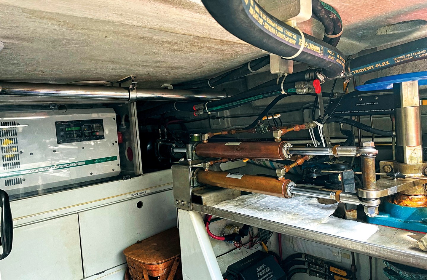 A detailed view inside a boat's lazarette showing the hydraulic steering assembly, rudder post, inverter, and overhead marine plumbing.