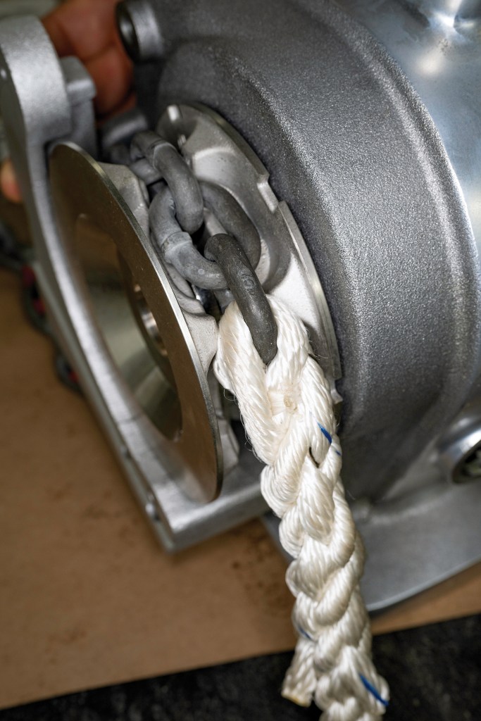 Close-up of a three-strand nylon rope spliced directly into a galvanized steel anchor chain link seated inside a windlass gypsy.
