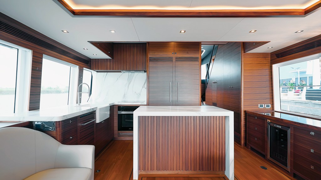 The modern galley of a Selene 64 Ocean Explorer yacht, featuring warm American walnut cabinetry, a waterfall quartz island, a farmhouse sink, and integrated high-end appliances.