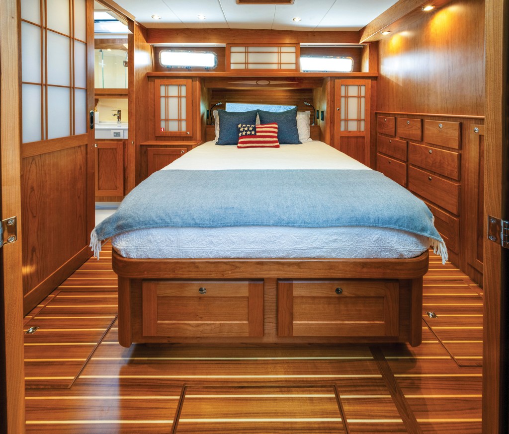 The master stateroom of a Sabre 51 Salon Express featuring a center island berth with integrated storage drawers, rich cherry wood cabinetry, sliding shoji-style doors, and teak-and-holly soles.