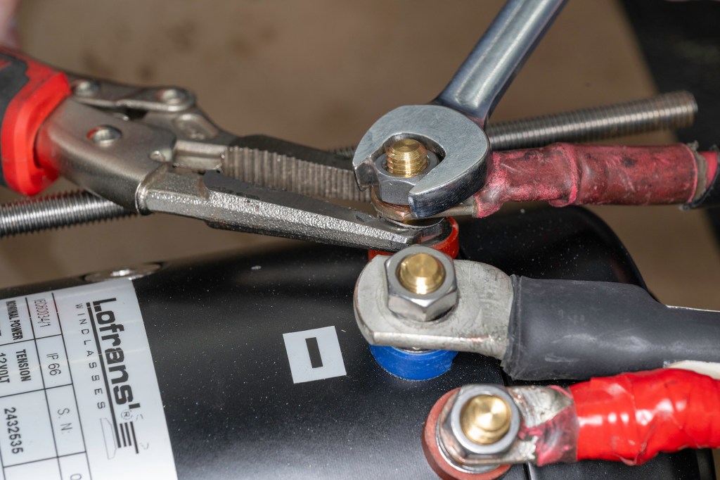 Using two wrenches to safely tighten a heavy-duty electrical terminal cable lug on a Lofrans windlass motor stud without twisting the internal connection.