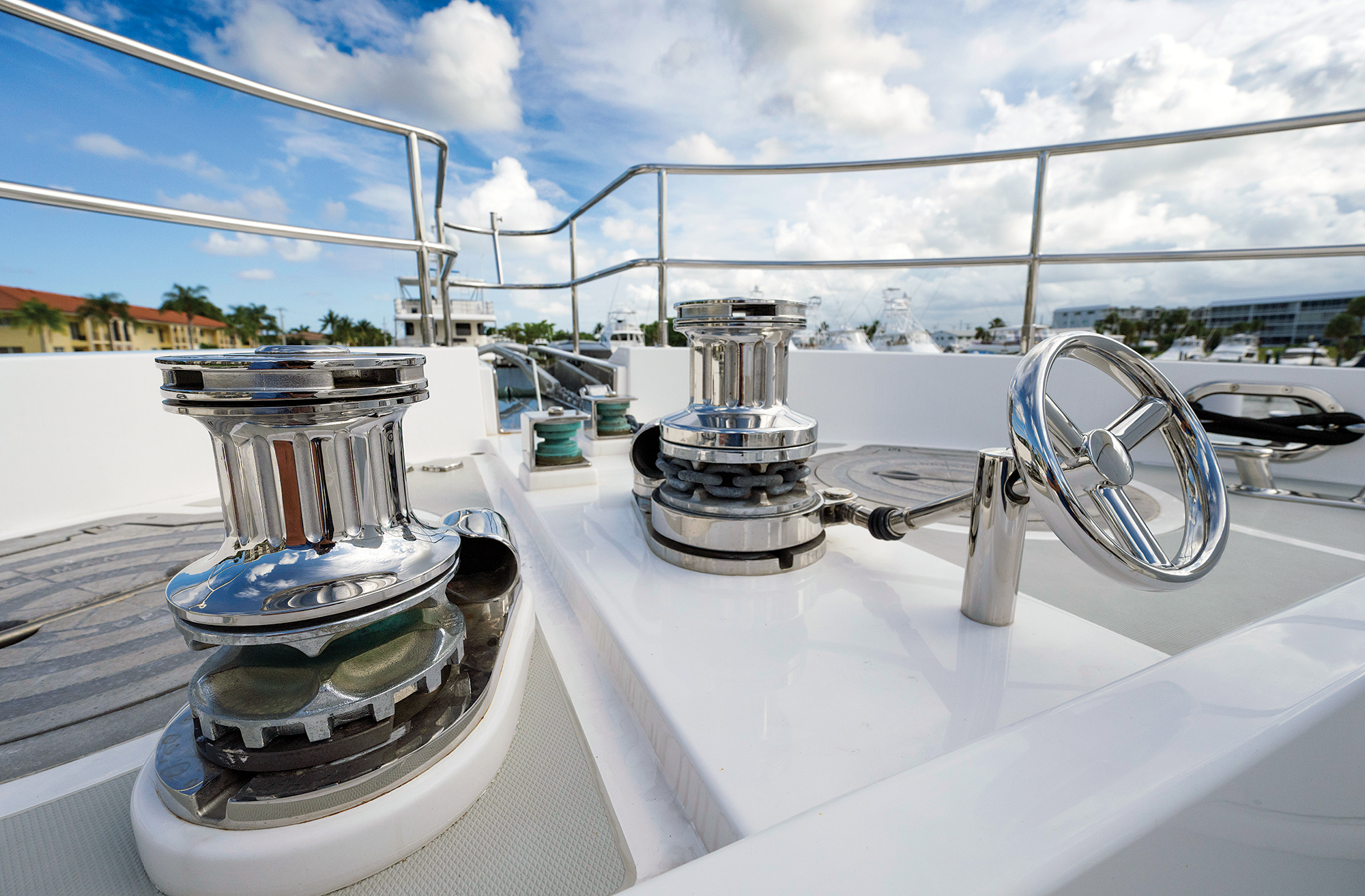 Alt Text: A close-up view of two polished stainless-steel windlasses and anchor gypsies mounted on the white foredeck of a yacht under a partly cloudy sky.
