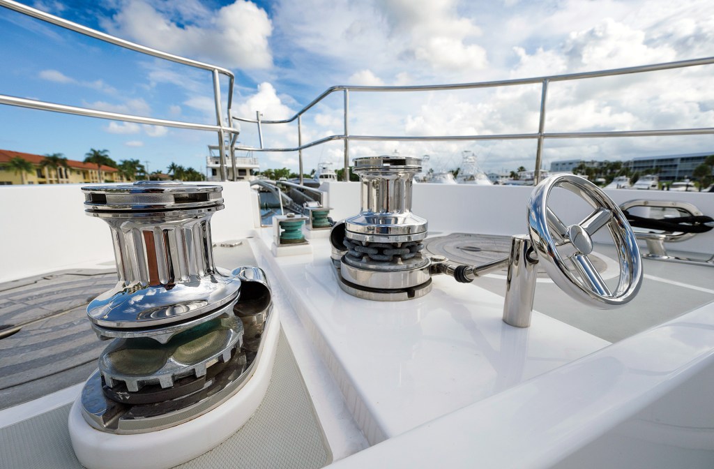 Alt Text: A close-up view of two polished stainless-steel windlasses and anchor gypsies mounted on the white foredeck of a yacht under a partly cloudy sky.