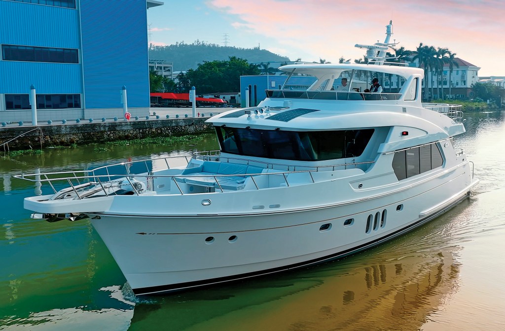 feat_Selene 64 Ocean Explorer A forward three-quarter view of the white Selene 64 Ocean Explorer yacht navigating a canal alongside shipyard buildings under a soft twilight sky.
