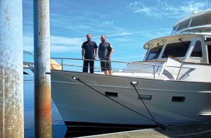 Twin delivery captains Assen and Nikolay Alexandrov standing on the bow deck of a motor yacht docked alongside a pier.