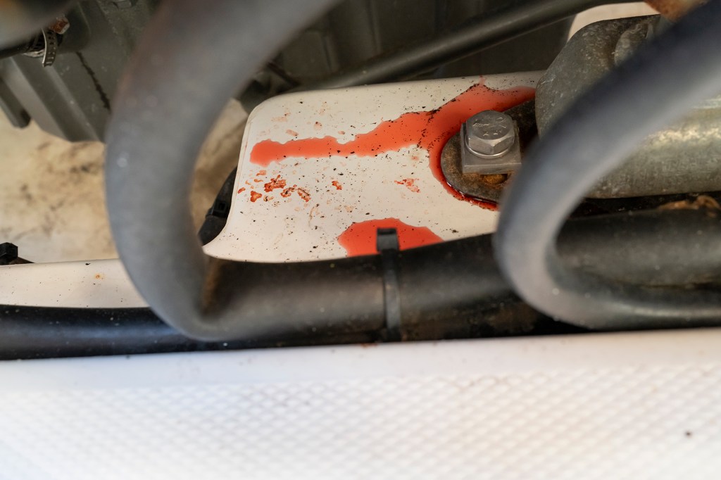 Close-up of red coolant fluid leaking onto a white engine surface behind black hoses in a marine engine room.