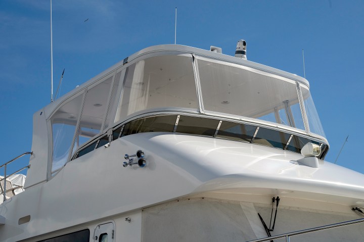 Yacht flybridge enclosed with crystal-clear rigid acrylic canvas panels mounted on tracks.