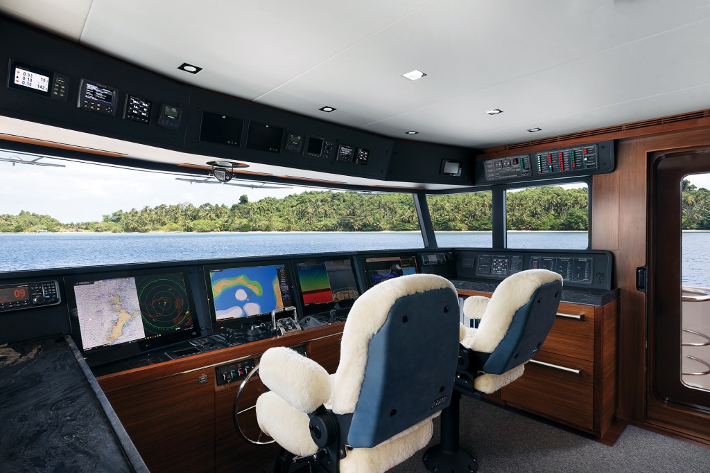 Pilothouse helm station of the Nordhavn 100 equipped with dual helm chairs, glass bridge navigation displays, and large forward-facing windows.