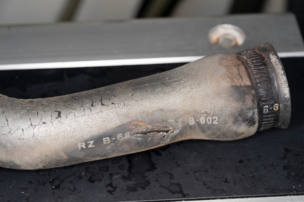 A cracked, worn black rubber marine engine hose with visible split along the side sitting on a dark surface.