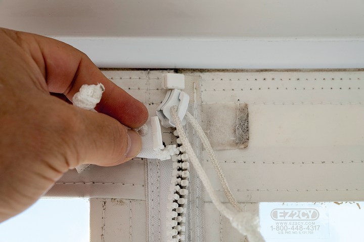 Close-up of a hand operating a boat canvas zipper with custom pull cords on an EZ2CY enclosure panel.