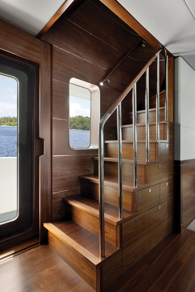Interior wooden staircase with stainless steel handrails and built-in storage drawers inside the Nordhavn 100 yacht.