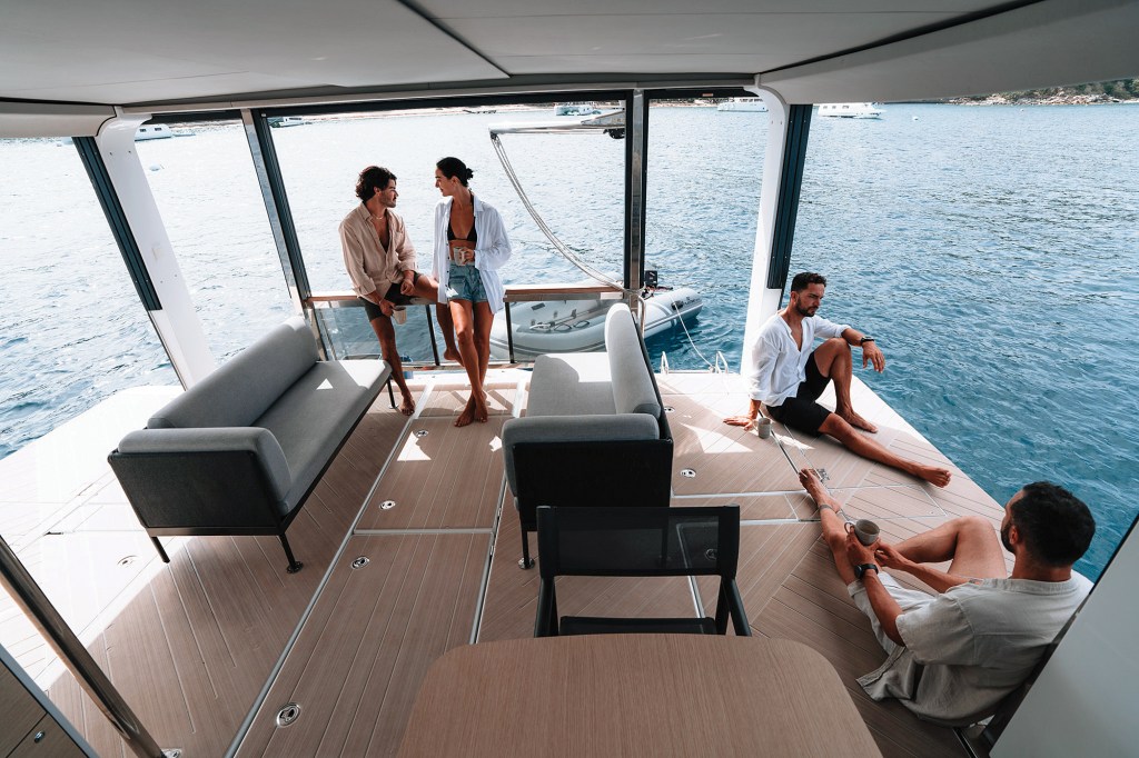 People relaxing on the spacious aft deck of the Jeanneau Sea Loft 480 with folded-down side bulwarks creating an expanded terrace over the water.