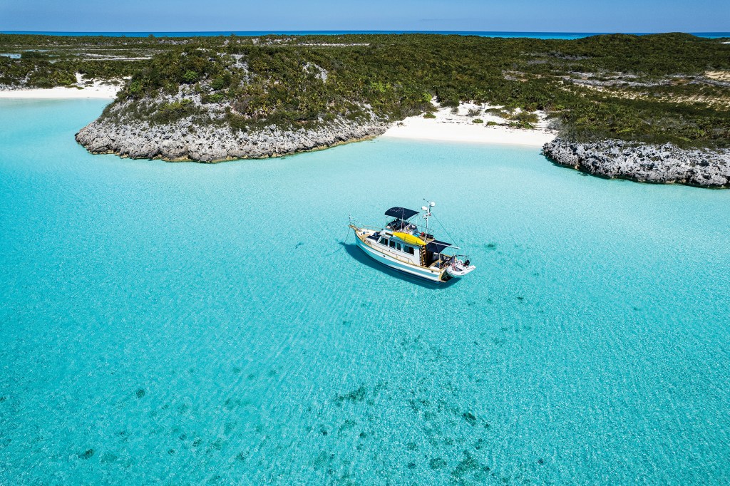 Aerial drone photograph of the restored Grand Banks 32 classic trawler Snow Goose anchored in crystal-clear turquoise Bahamian waters.