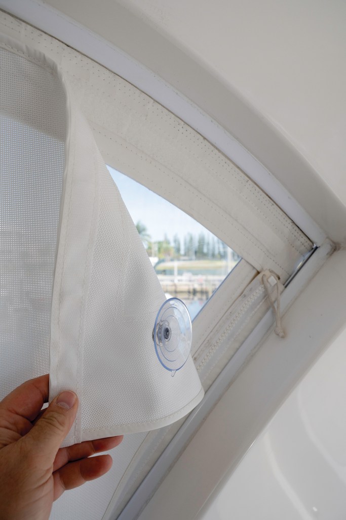 Hand peeling back a white mesh boat sun screen attached with a clear suction cup to a clear enclosure panel.
