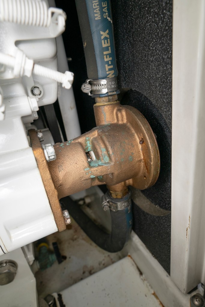 A bronze marine raw-water pump showing blue-green corrosion at the shaft and connected to black reinforced hoses.