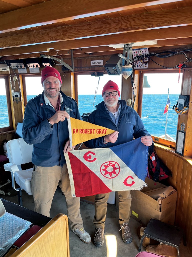 Captain S. Davis Alford and crew member holding RV Robert Gray flags inside the pilothouse.