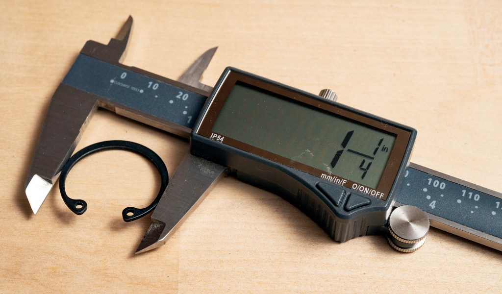 Digital caliper measuring the diameter of a black retaining ring on a wooden workbench.