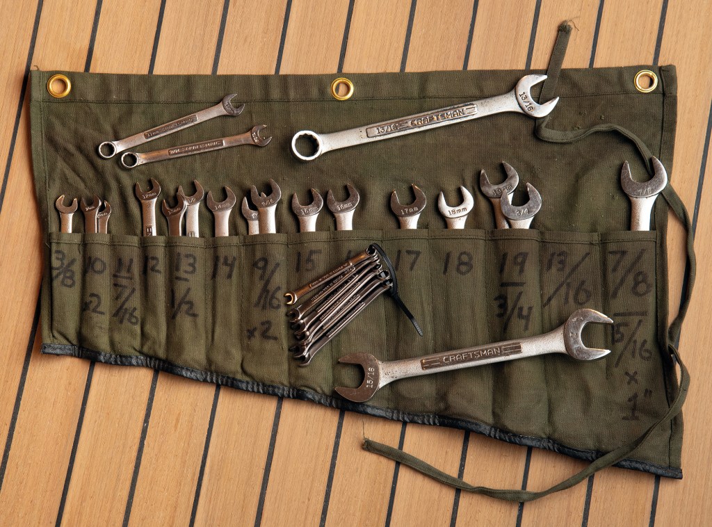 Canvas wrench roll organizer filled with combination wrenches and Allen keys laid flat on a teak boat deck.