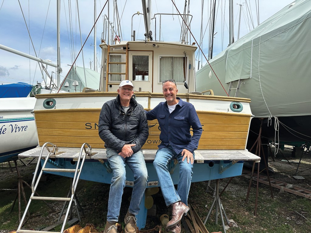 Photographer Onne van der Wal sitting on the stern swim platform of his trawler Snow Goose alongside a friend in a boatyard.
