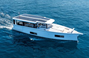feat_jeanneau-sea-loft-480 A white Jeanneau Sea Loft 480 monomoran yacht cruising across blue open water, showing its solar-panel roof, open deck salon, and sunbed on the bow.