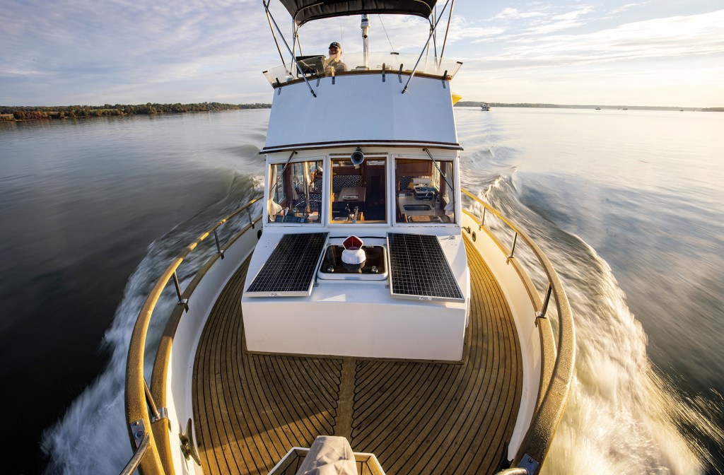 Bow view looking back toward the flybridge of a restored Grand Banks classic trawler yacht cruising on calm open water at sunset.
