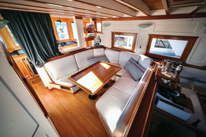 Interior salon of the classic motor yacht Paspatoo featuring a wooden dining table, U-shaped white settee, and rich teak trim.