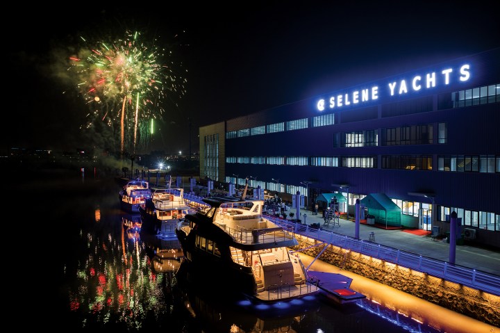 Fireworks light up the night sky over the illuminated Selene Yachts shipyard facility with yachts docked along the waterfront quay.
