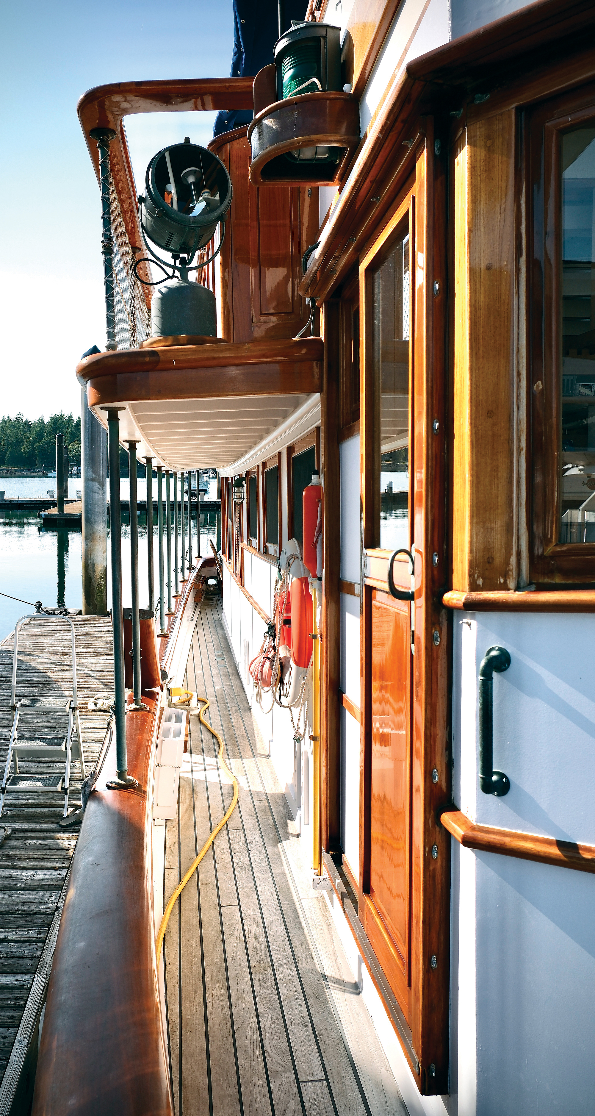 Teak side deck and varnished caprails of the historic motor yacht Paspatoo showing a vintage Carlisle & Finch searchlight.