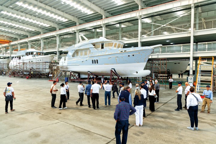 A group of visitors tours the vast Jet-Tern shipyard hangar, viewing Selene yachts under construction on the assembly line.