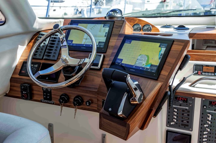 The helm station of an Aspen C110 featuring dual Garmin touchscreens, a stainless steel steering wheel, throttle controls, and wood accent paneling.