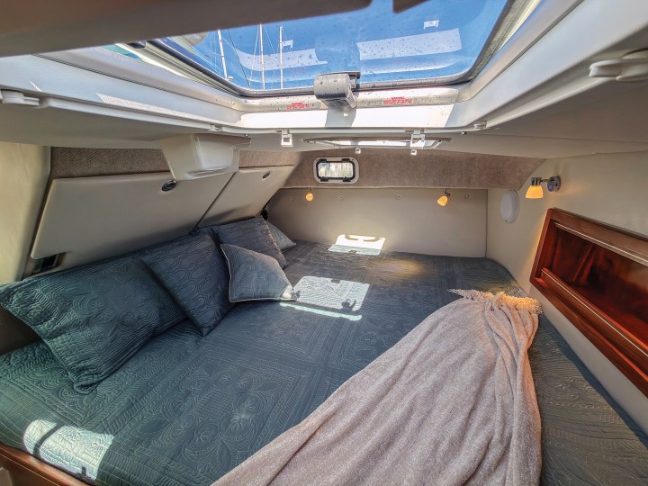 The forward master stateroom on an Aspen C110 featuring a king berth, blue bedding, reading lights, and an overhead deck hatch.