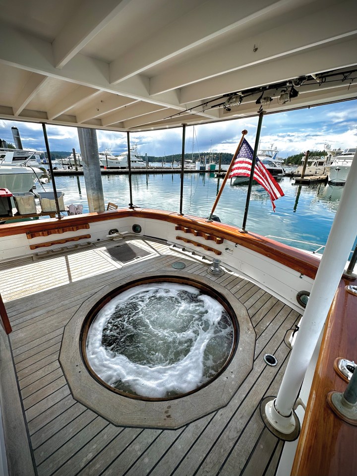 Covered aft cockpit of the classic motor yacht Paspatoo featuring a custom teak hot tub integrated into the wooden deck facing the marina.