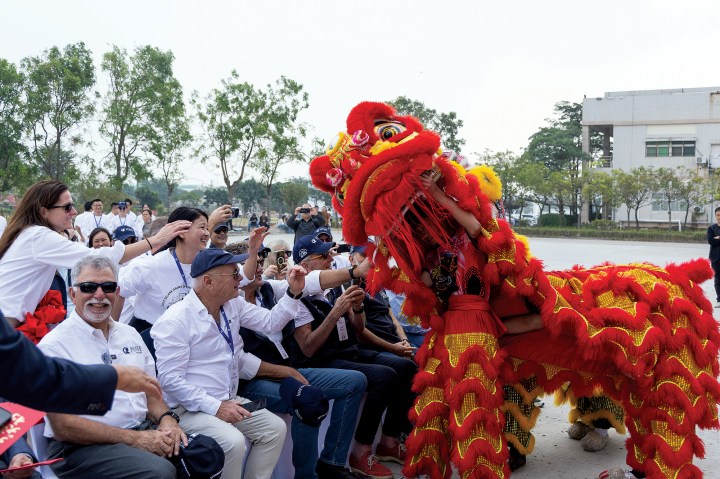 A vibrant red and gold Chinese dragon dancer performs in front of a crowd of seated guests at an outdoor event.