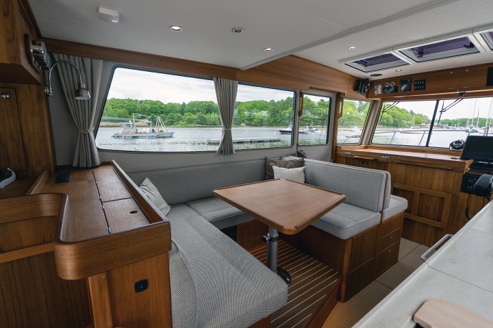 The convertible dinette seating area in the Targa 41 salon with a wooden table, large windows, and teak cabinetry.