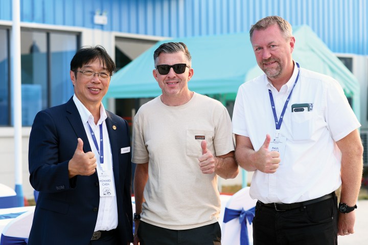 Selene Yachts founder Howard Chen giving a thumbs-up alongside two event attendees outdoors.