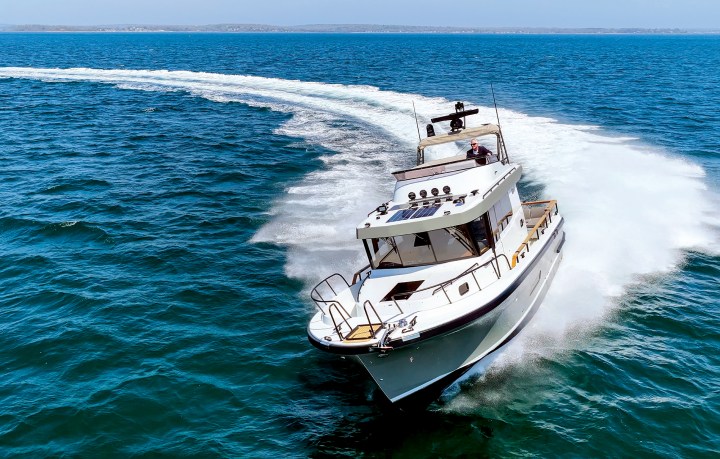 An aerial front view of a Targa 41 motor yacht executing a sharp turn at high speed on bright blue open water.