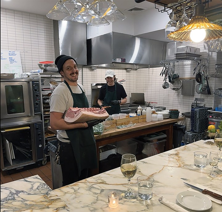 Chef Dave Mountain smiling while presenting a large cut of raw meat inside the open kitchen at Dave the Butcher in Beacon, New York.