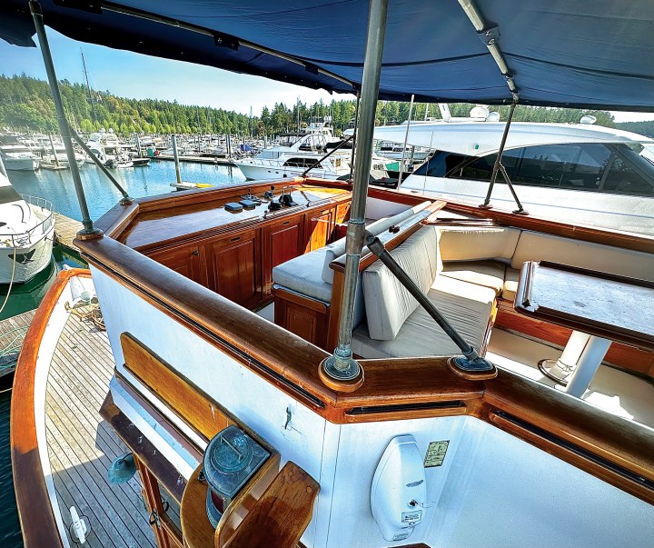 Shaded flybridge seating area and upper helm console of the classic motor yacht Paspatoo framed by varnished teak caprails.