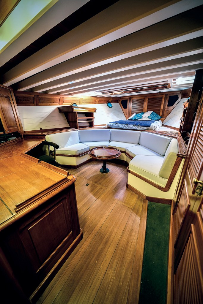 Spacious master stateroom onboard the classic motor yacht Paspatoo featuring custom woodwork, exposed ceiling beams, a curved settee, and an elevated berth.
