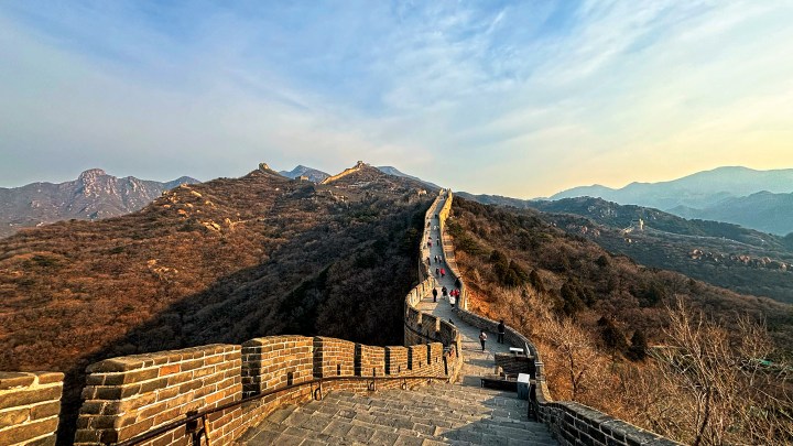 Panoramic view of the Great Wall of China winding along rugged, sunlit mountain ridges.