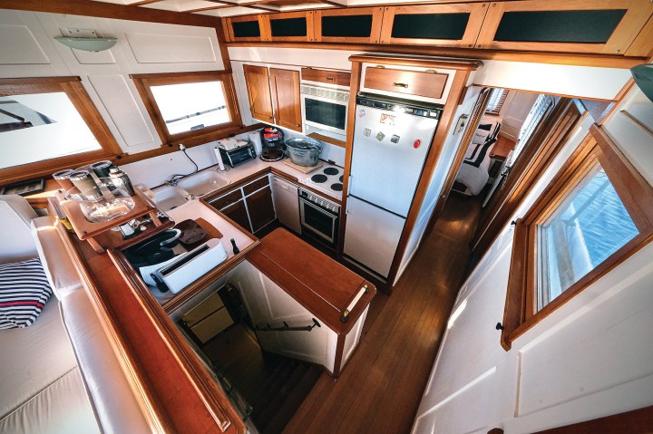 Fully equipped galley aboard the classic motor yacht Paspatoo featuring custom wooden cabinetry, full-size refrigerator, stove, and companionway stairs.