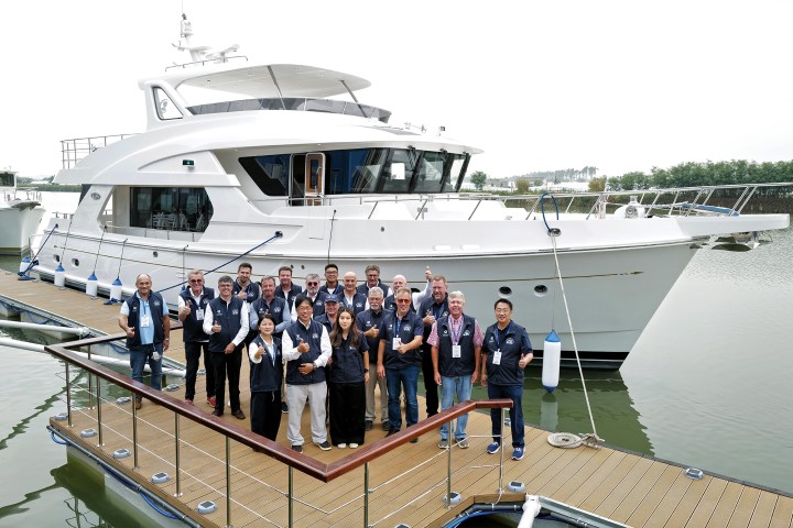 A large group of Selene Yachts team members and owners posing on a floating dock in front of a new white yacht.