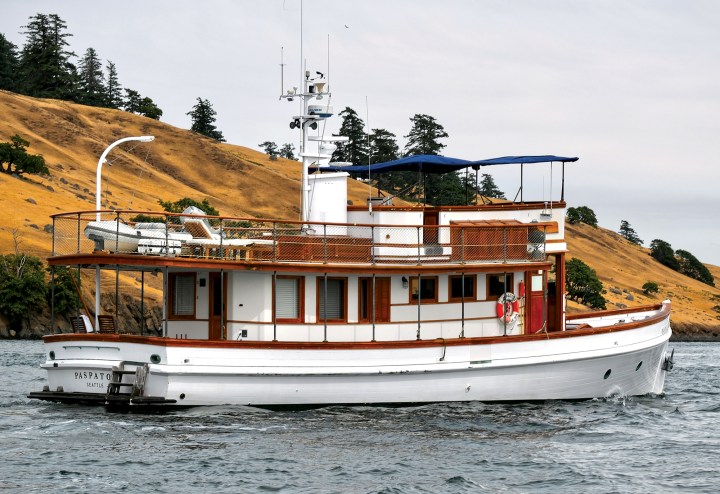 Three-quarter stern view of the classic wooden motor yacht Paspatoo underway with a bimini-shaded flybridge and upper deck davit.