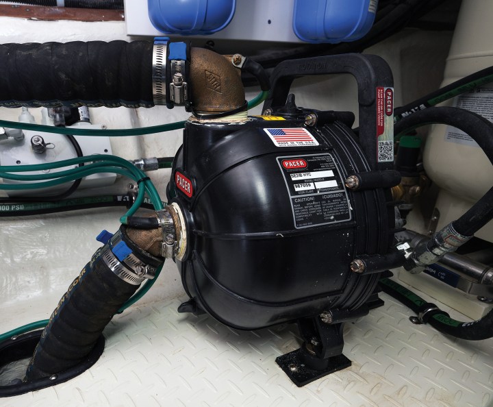 A heavy-duty black Pacer hydraulic dewatering and bilge pump secured to a diamond-plate floor in an engine compartment with reinforced hoses and brass fittings.