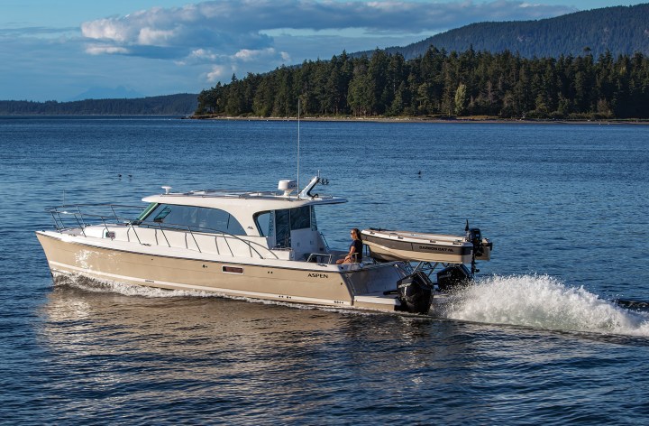 An Aspen C110 power catamaran cruising on open water carrying a tender dinghy mounted on the stern davit system.